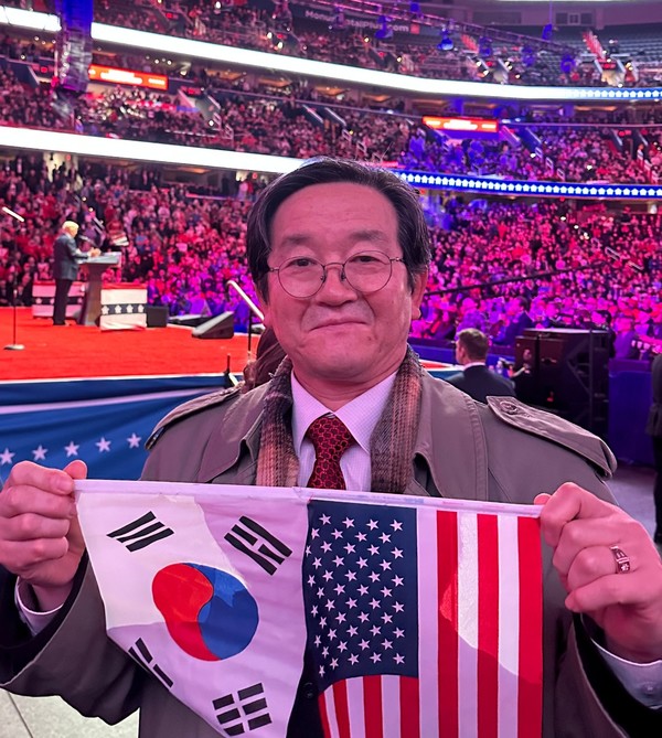 김회창 목사(엘에이 말씀새로운교회 · 사진)가 도널드 트럼프 미국 47대 대통령 취임식에 초청받아 참석했다.. 태극기와 성조기는 손에든 김회창 목사  뒤 강단에  트럼프 대통령이 연설하고  있다..